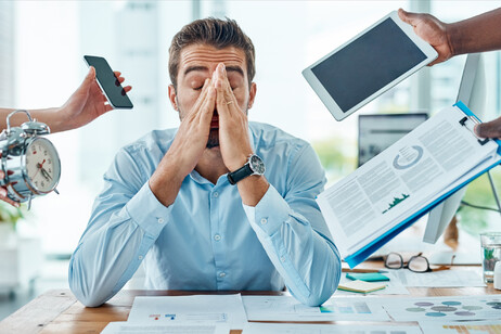 Un uomo alla scrivania sollecitato da molte incombenze foto iStock.